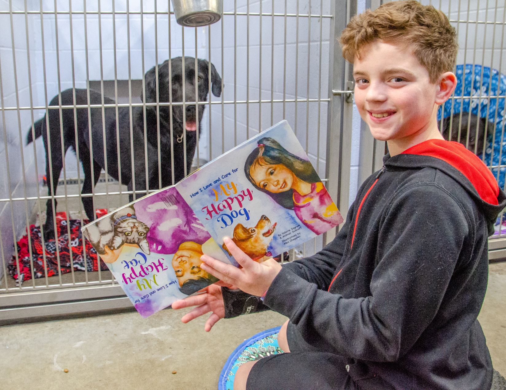 Red haired child reading a children's book to a black shelter dog at OHS Salem