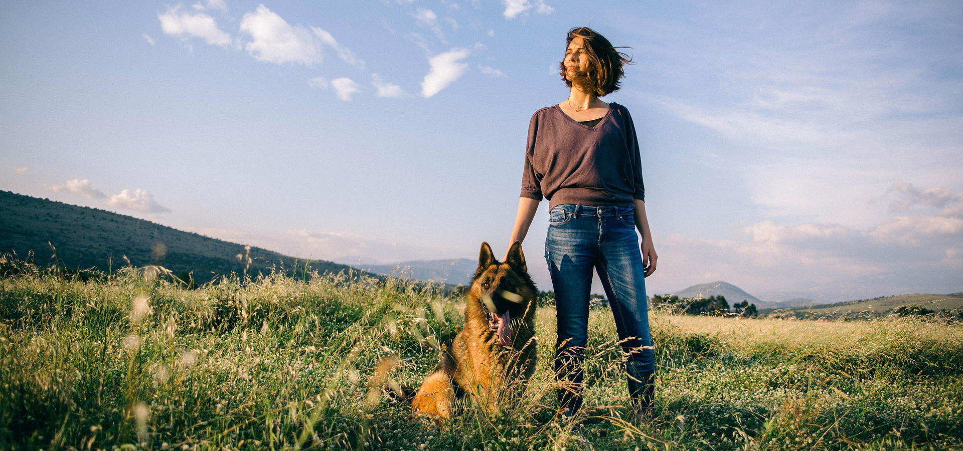 Woman with german shepherd standing in a meadow together.