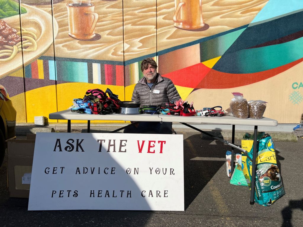 Dr. Mack at Blanchet House with pet supplies and an "Ask the Vet" sign